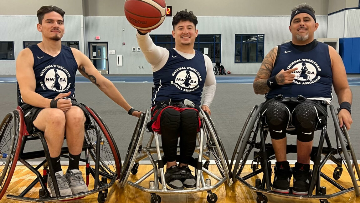 Three men in wheelchair basketball chairs wearing National Wheelchair Basketball Association shirts (left to right, Jorge, Artur, and Armando) pose on the court with a basketball.